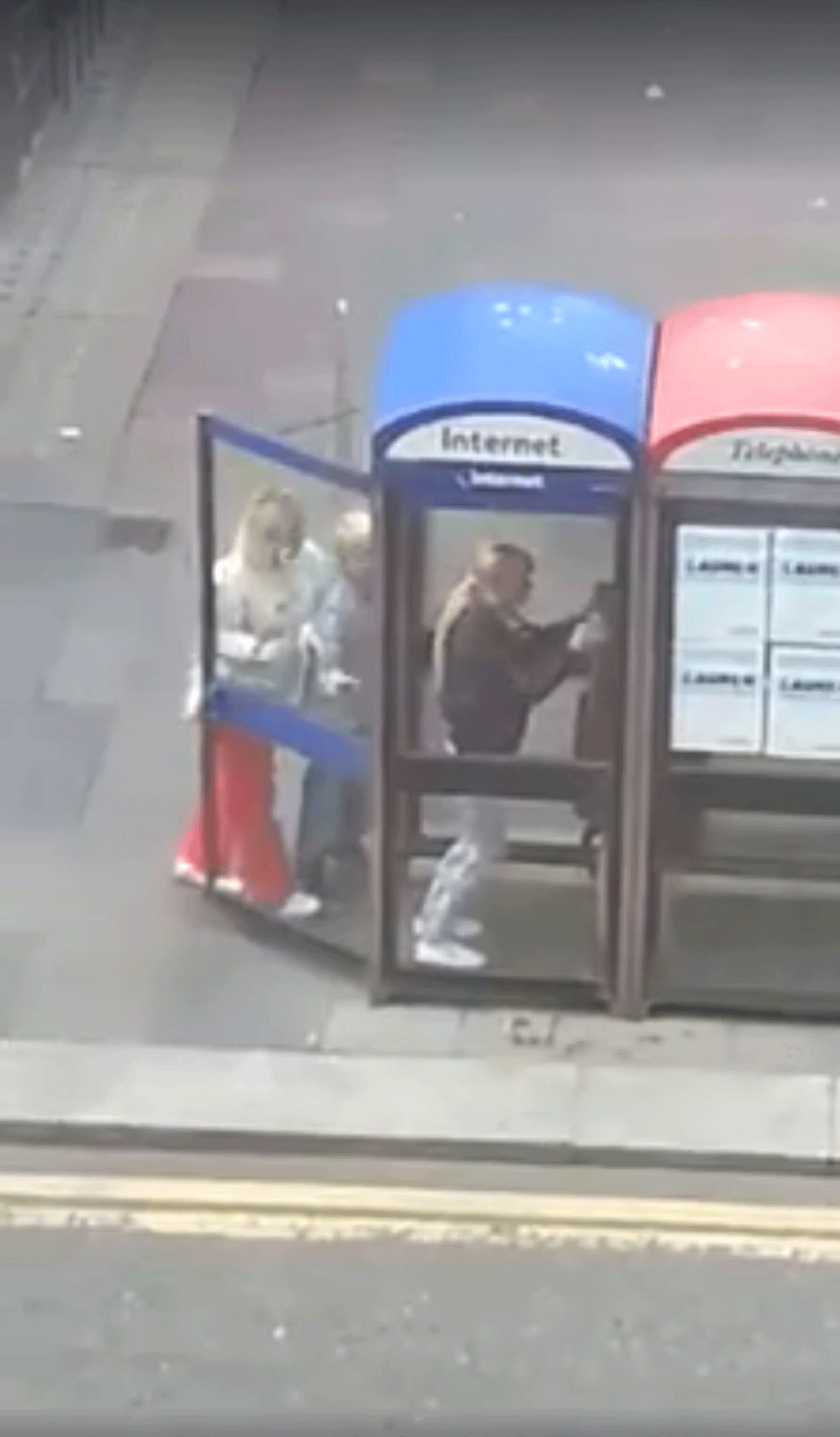 The woman and the boy take turns to grab the frame of the phone box with both hands so they can kick it