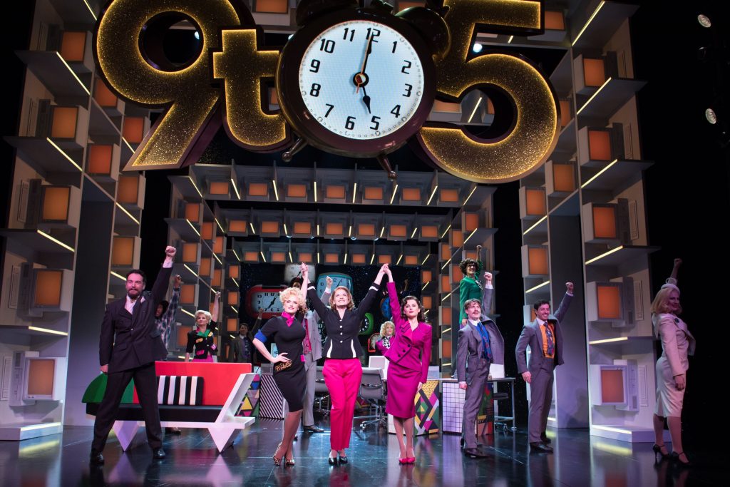 The image shows the cast of the West End production of 9 to 5 The Musical.