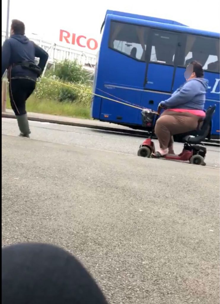 Man pulls woman on mobility scooter with a rope