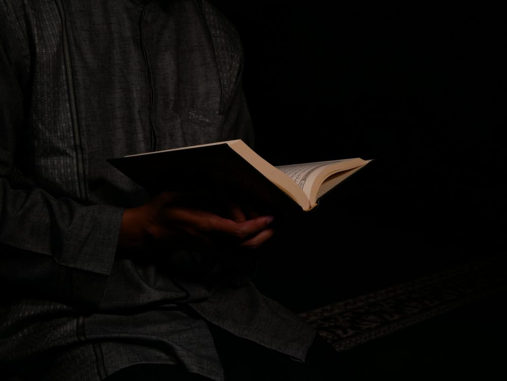 A person reading the holy Quran in a low light room.