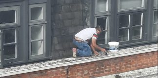 An image of the painter working on the window ledge of a five-storey building.
