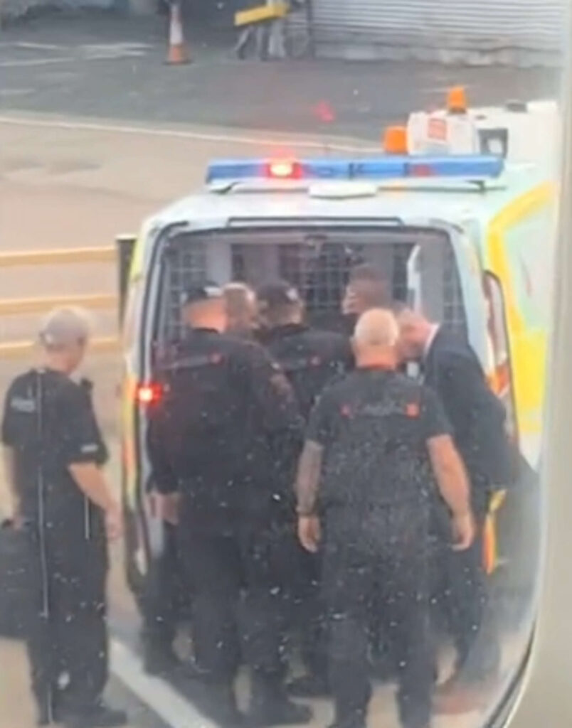 The man being put into the back of a police van.