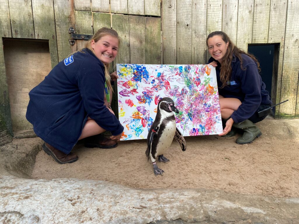 Squidge stands alongside his painting, held by two animal carers.