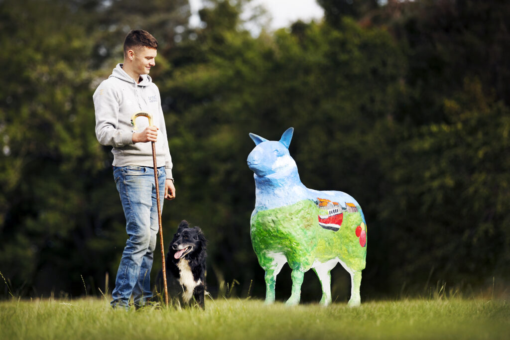 A shepherd standing alongside a sculpture with his dog.