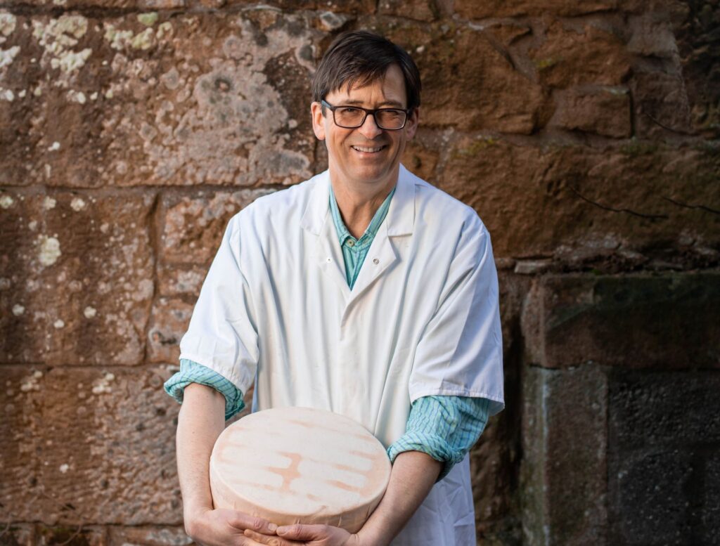 Highland Fine Cheeses Owner Rory Stone posing with a wheel of cheese from the cheesemaker.