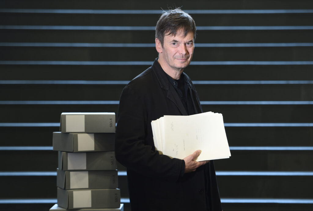 Ian Rankin holding a book, surrounded by some of the material he donated to the library.