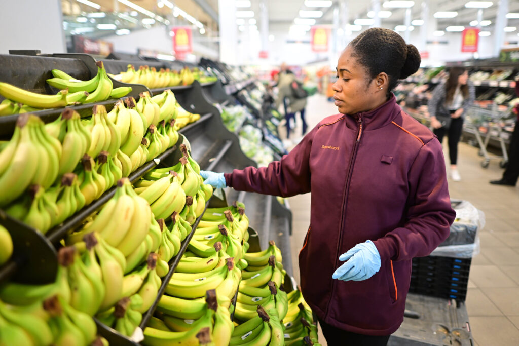 Sainsbury's colleague sorting bananas in the fruit aisle of a store.