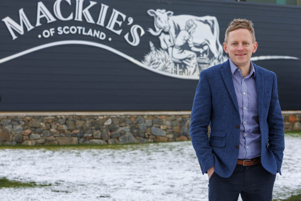 Stuart Common stood outside in from of Mackie's of Scotland sign