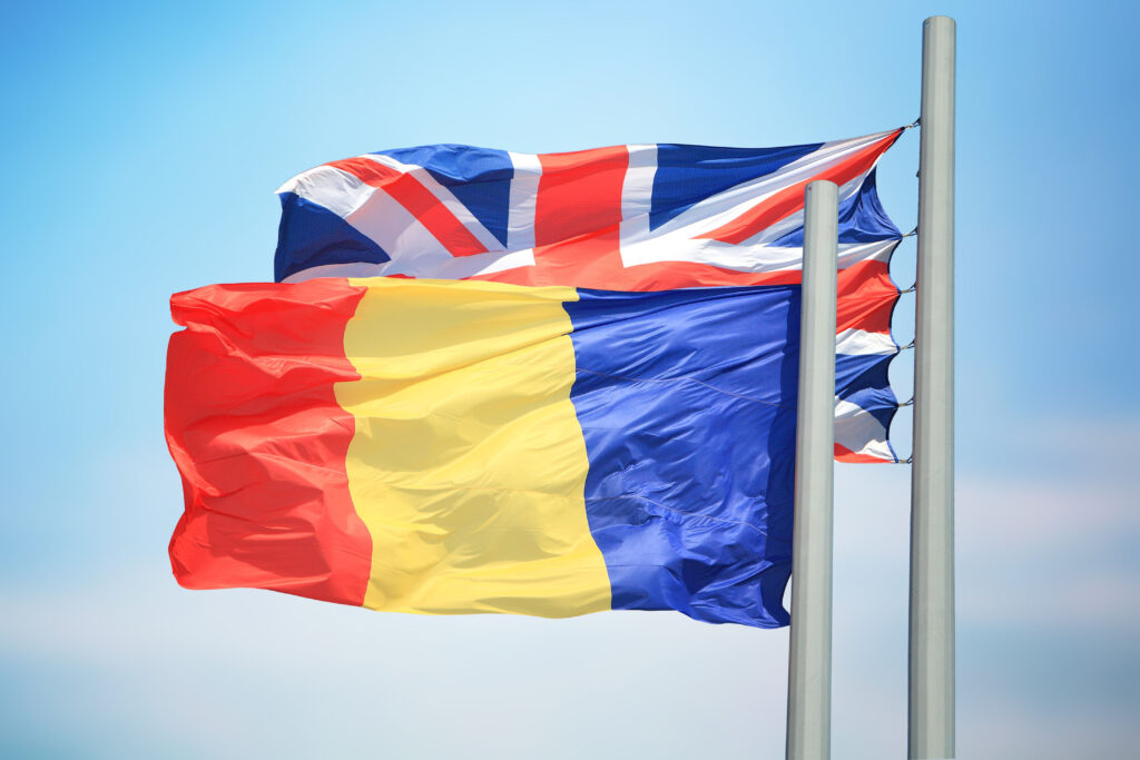 Romanian flag and Union Jack flying on background of blue skies.