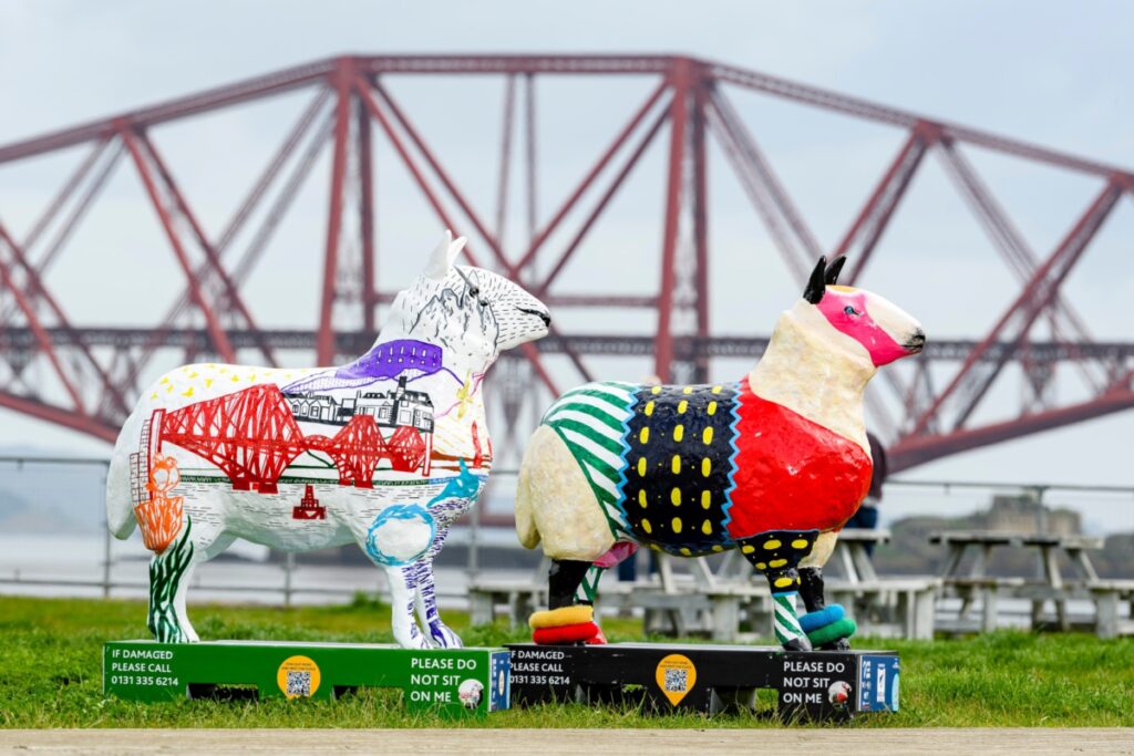 Two decorated sheep statues, backdropped by Forth Bridge