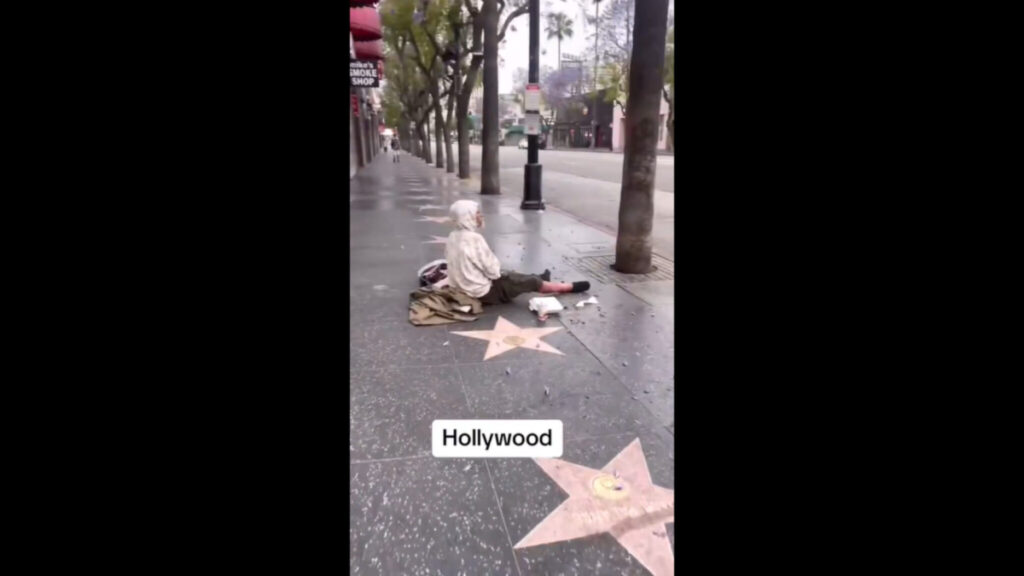 Homeless man sitting on the ground at the Hollywood Walk of Fame in Los Angeles, California.