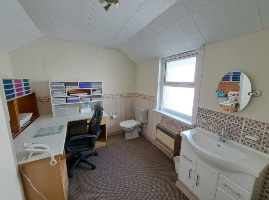 The office sits next to the toilet and a sink