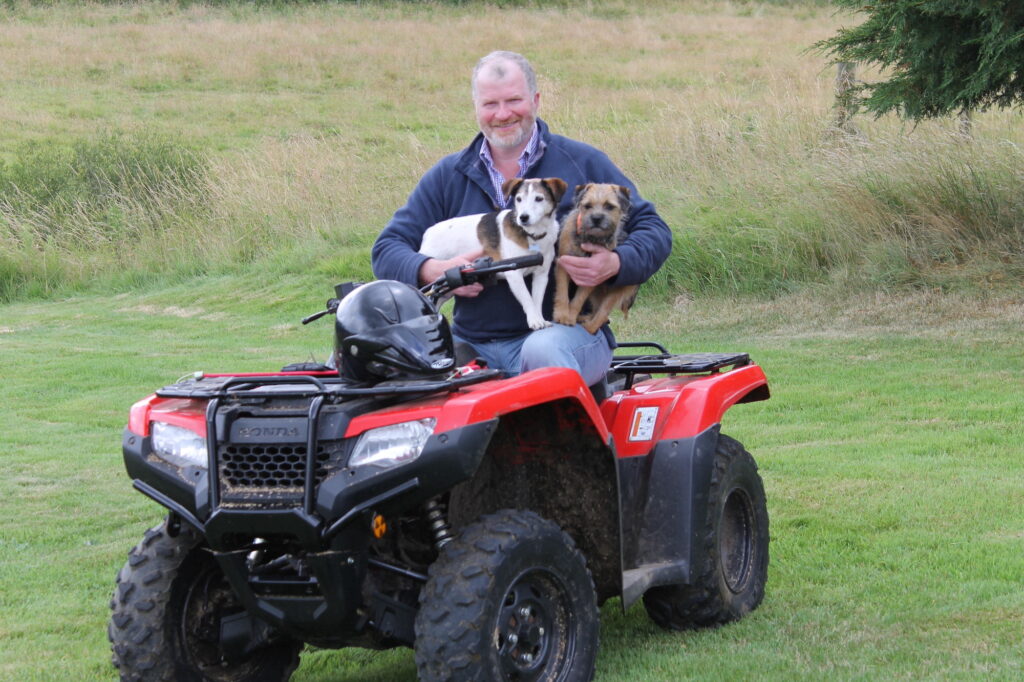 Doug Bell, sitting on a quad bike with two dogs.