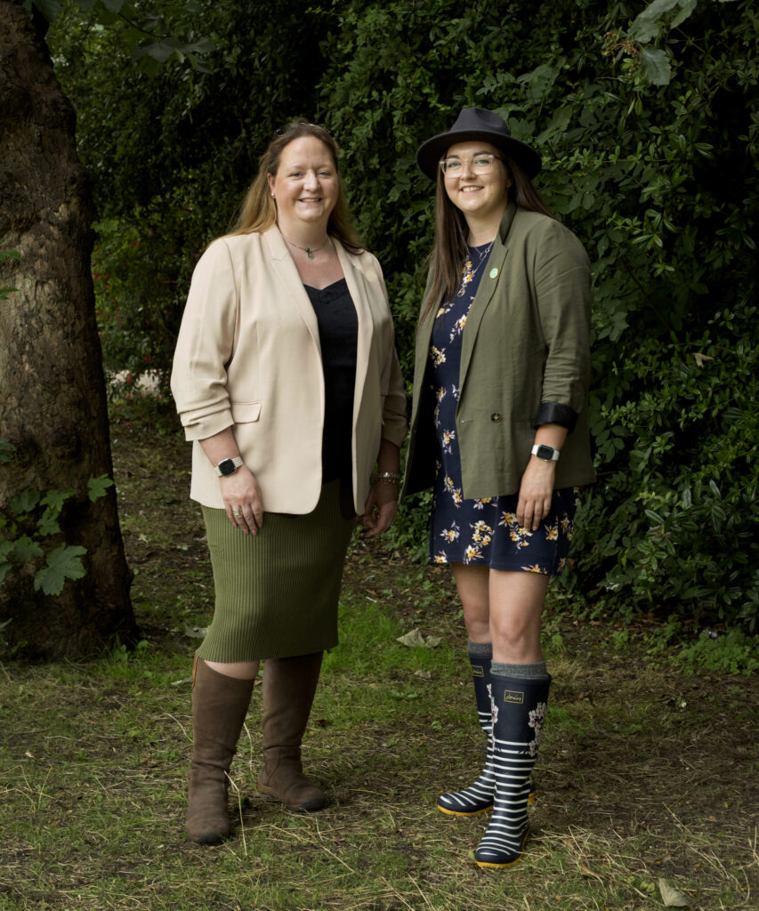Two women smile as they pose in farming clothes and wellies