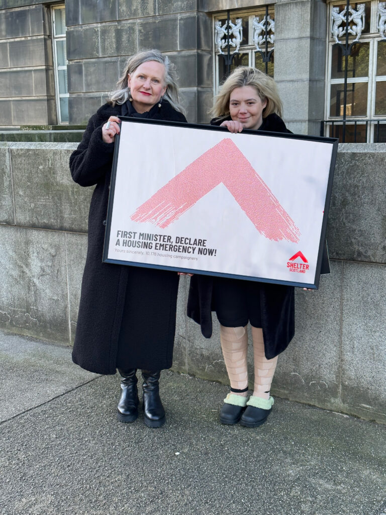 Alison Watson (left) holds sign with client Stacey Grieve (right) urging the First Minister of Scotland to declare a housing emergency now.