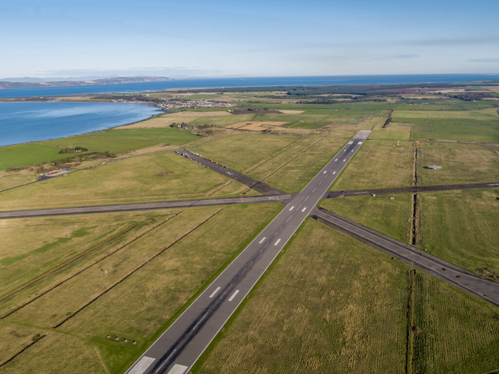 Aerial drone photo of runway at Inverness Airport by the water.