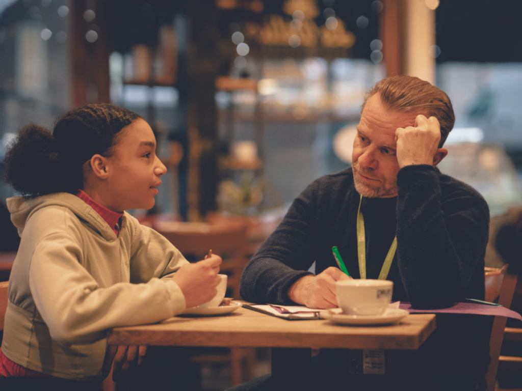 A young girl and a man from Barnardo's are talking in a coffee shop.