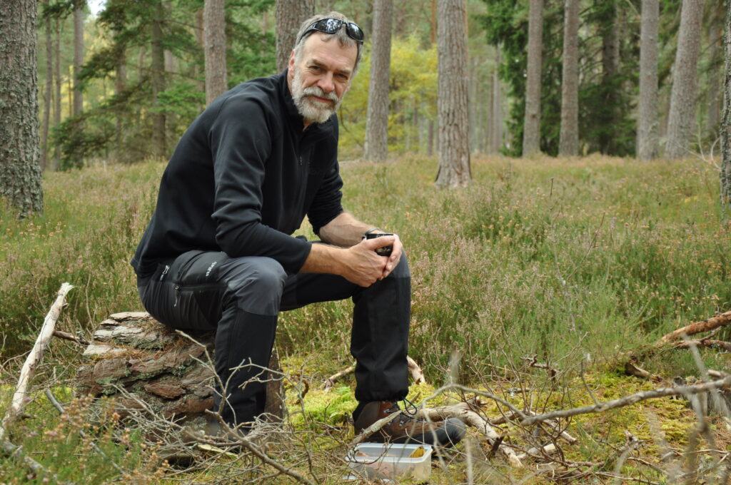 Dr Andrew Taylor sits on a log in the forest