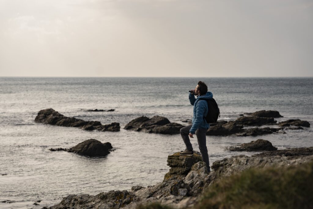 Chris Lawlor looks out at the Atlantic from a rocky coast whilst taking a nip from his hip flask
